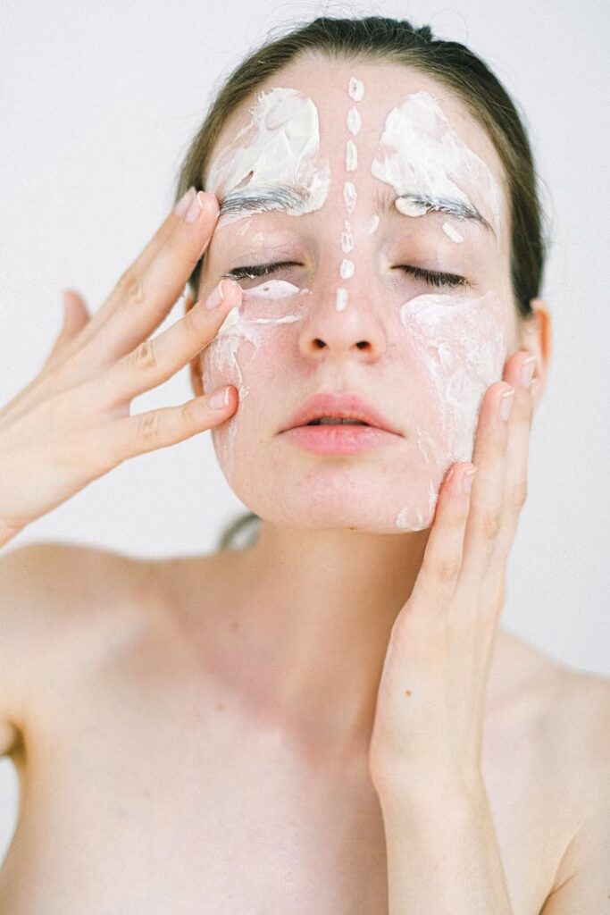 Young woman with skincare cream on face, eyes closed, in studio.